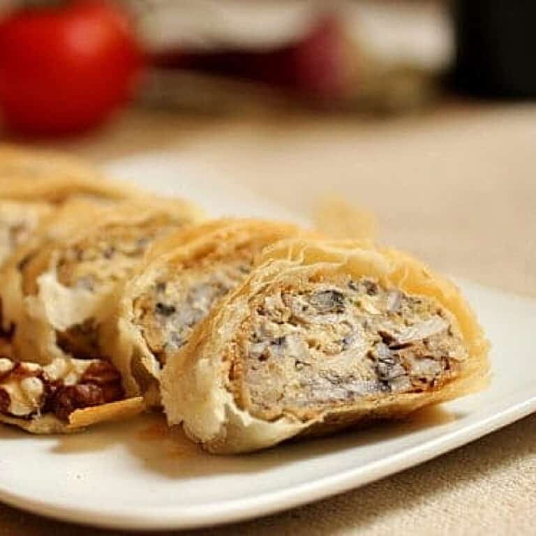 Slices of mushroom strudel on a white plate with beige surface.