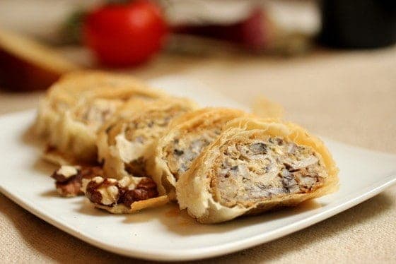 Close up of mushroom strudel slices on a white plate with a beige background.