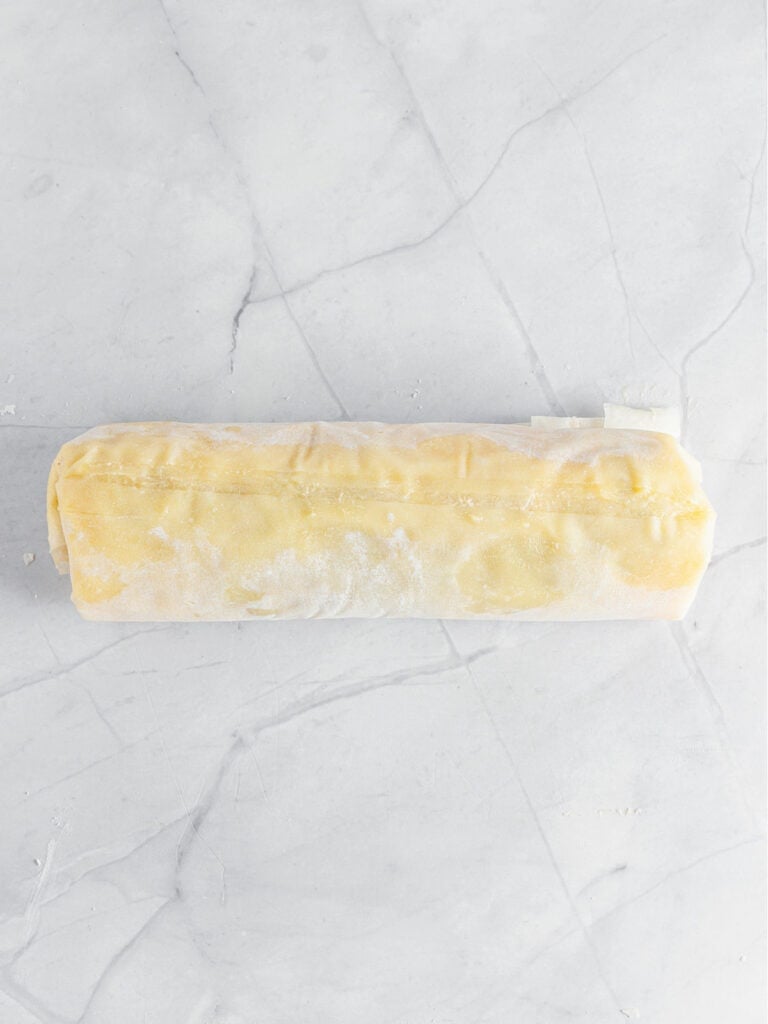 Rolled phyllo dough strudel before baking on a white marble surface.