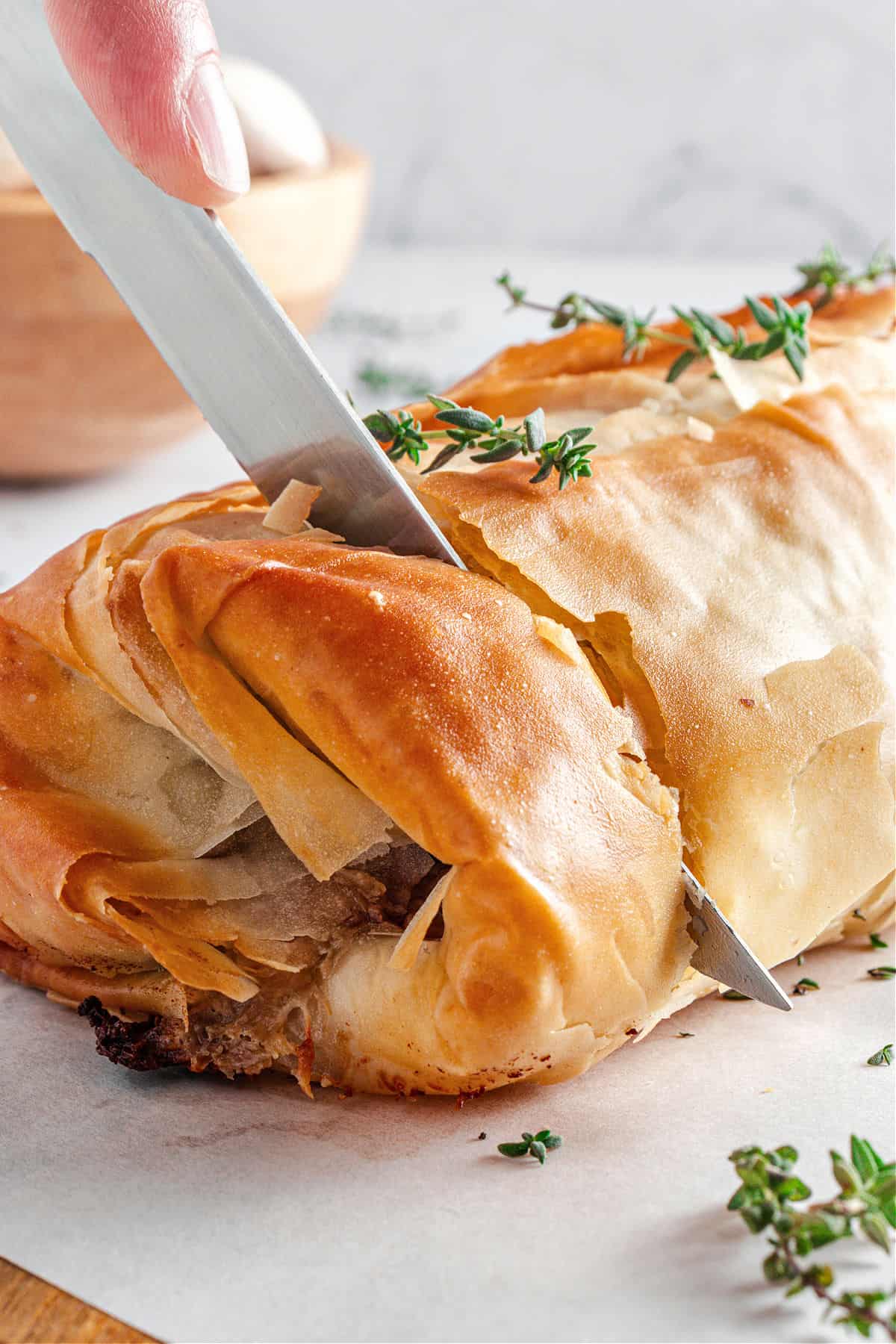 Cutting phyllo mushroom strudel with silver knife. Light gray background. Thyme sprigs.