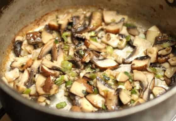 Skillet with mushrooms and green onion being cooked.