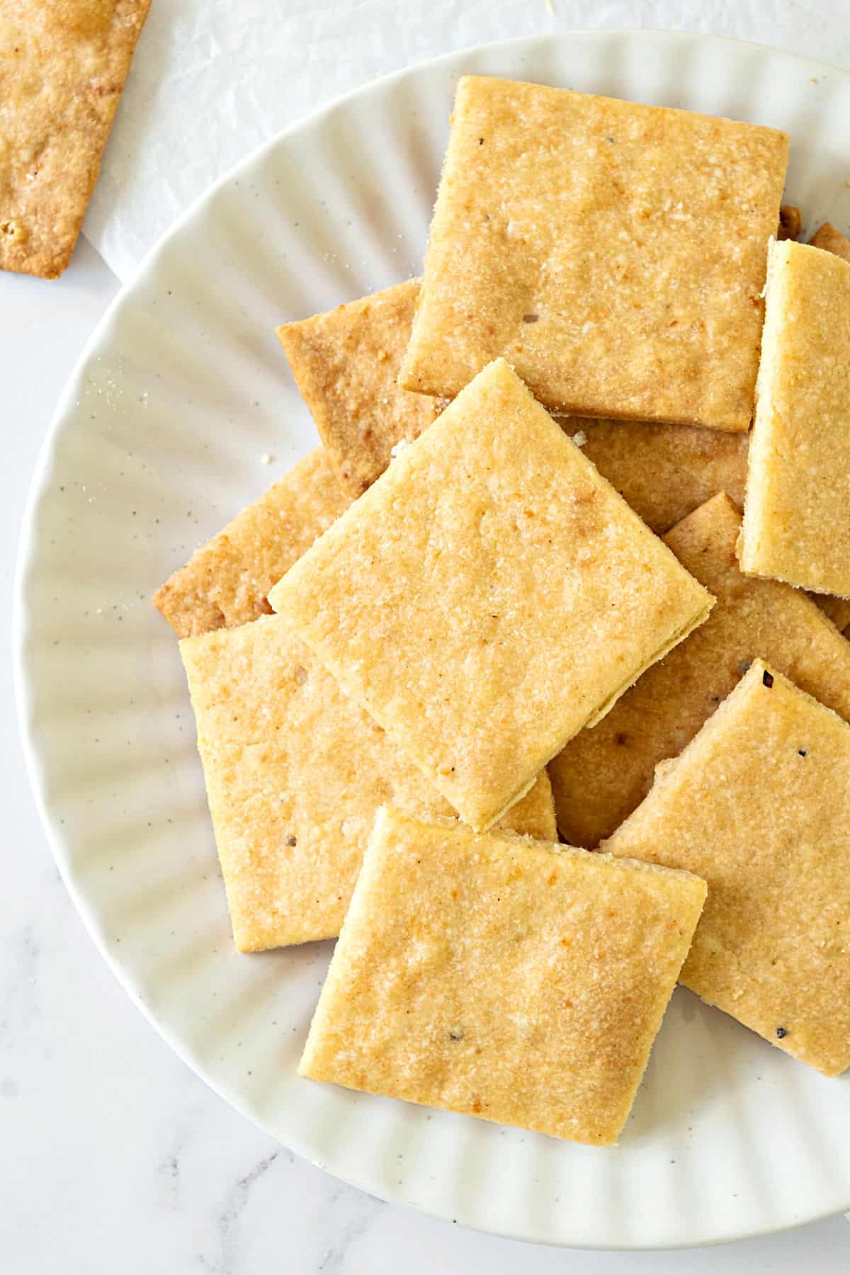 Partial view of white plate with pile of cheese crackers. White surface.