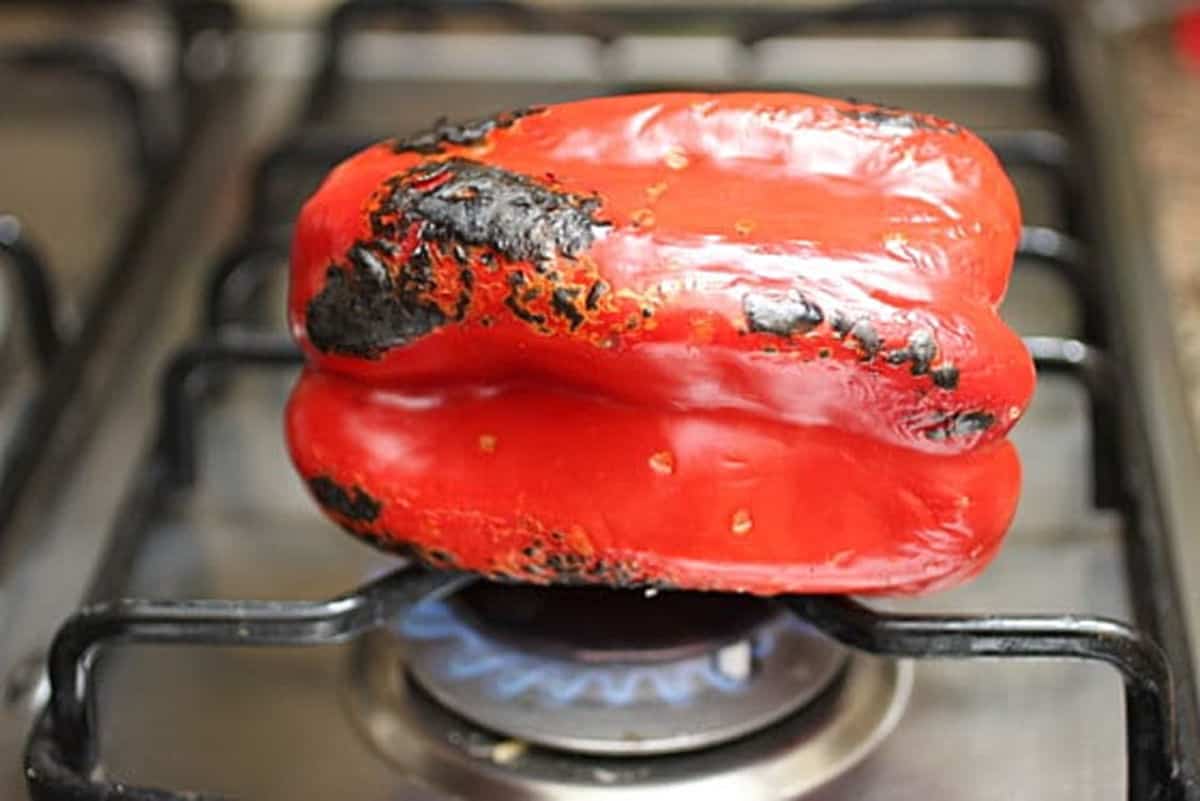 Charring a whole red pepper directly on the stove.