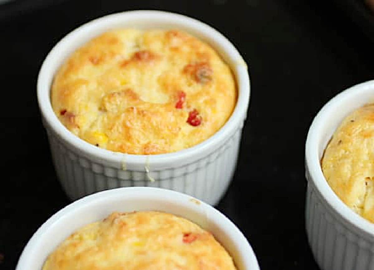 White ramekins with corn pudding on a black metal tray.