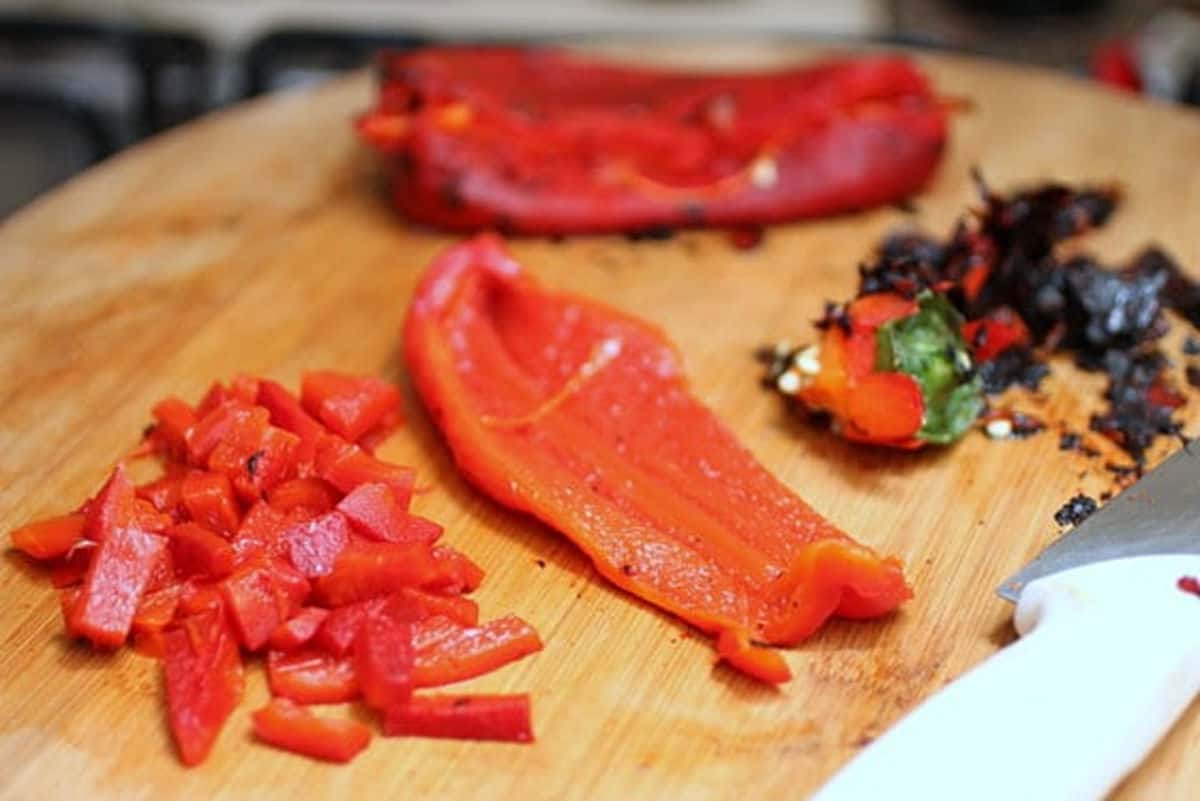 Cutting pieces of roasted red pepper on a bamboo wooden board.