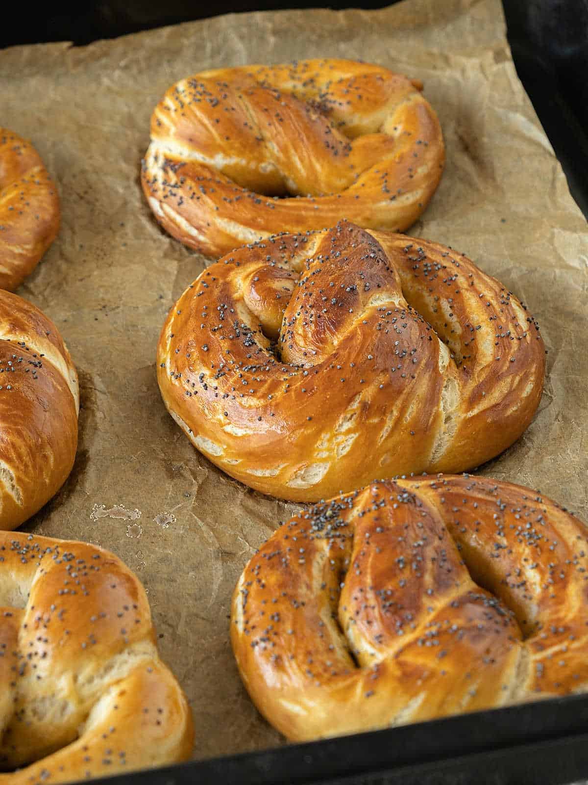 Beige parchment paper on a black tray with baked soft pretzels.