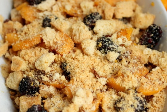 Croutons over peaches and blackberries in white dish. 