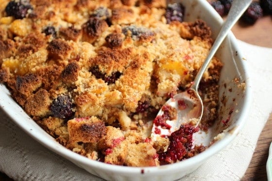 Baked peach blackberry Brown Betty in white oval dish with silver spoon inside. 