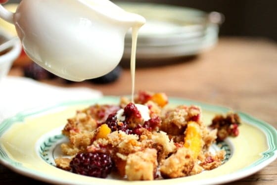 Peach Blackberry Brown Betty on yellow and green plate with cream pouring over it from a jar. 