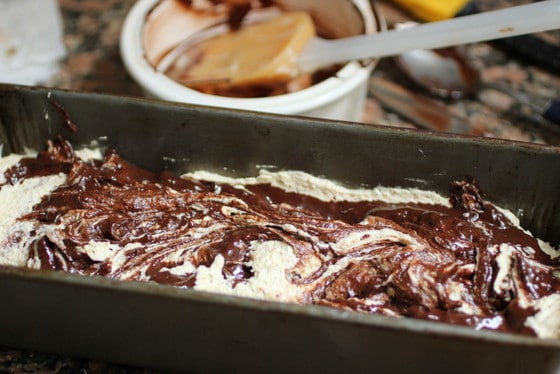 Unbaked loaf cake with chocolate swirl on metal pan. A spatula in bowl in the background. 