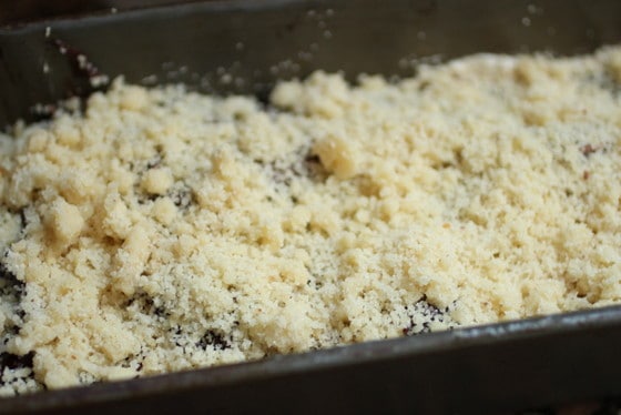 Streusel over cake batter in a rectangular dark metal pan. 