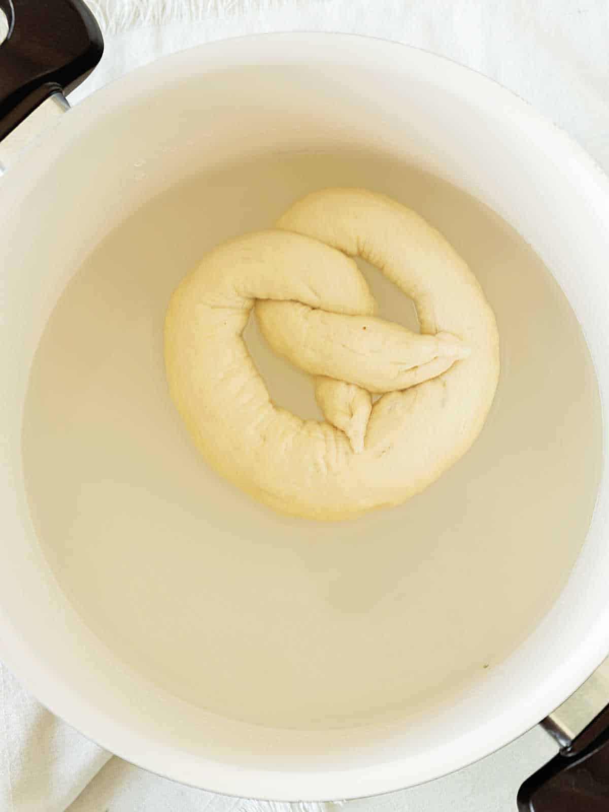 White pot with pretzel being boiled.