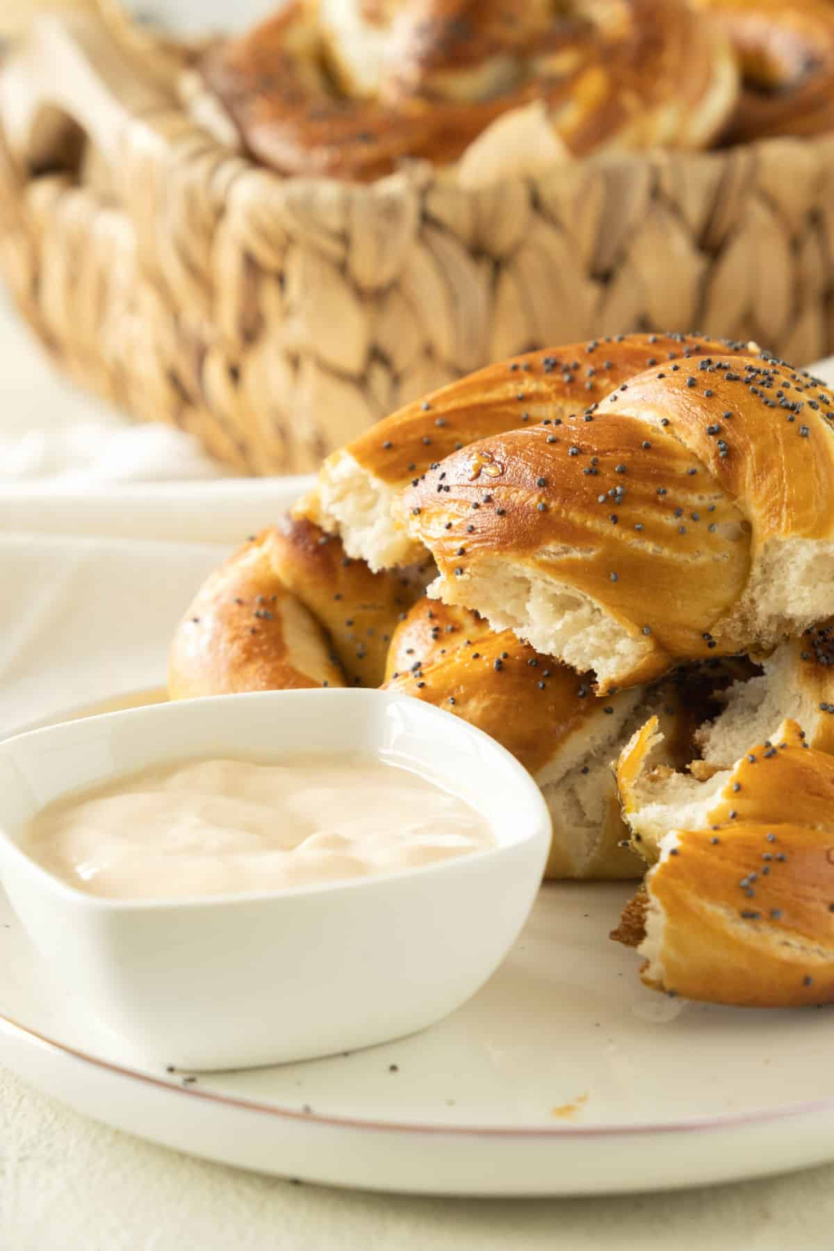 Pieces of soft pretzels on a white plate with cheese sauce in a bowl. Basket in the background.
