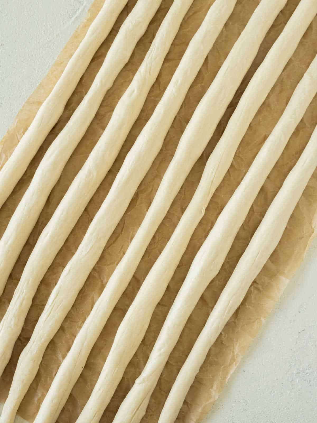 Thin ropes of pretzel dough on beige parchment paper.