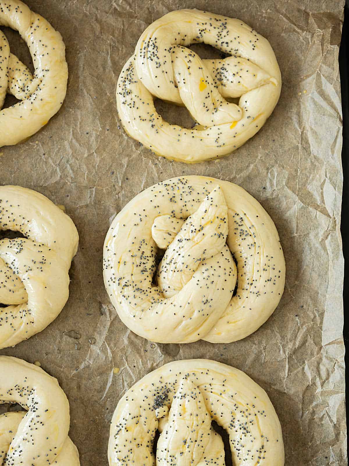 Poppy seed topped pretzels before baking on beige paper.