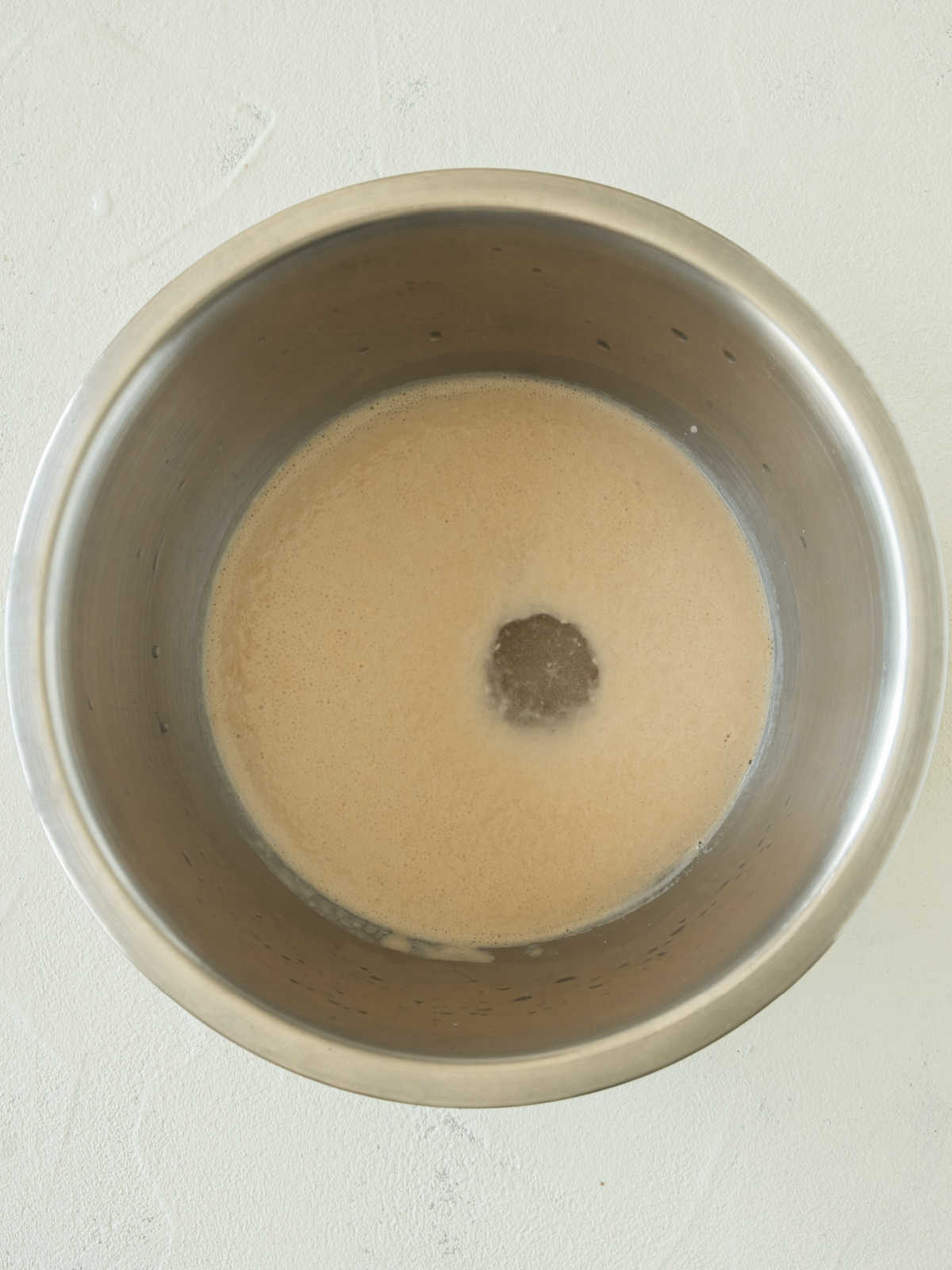 Yeast foaming with water in a metal bowl. Whitish gray surface.