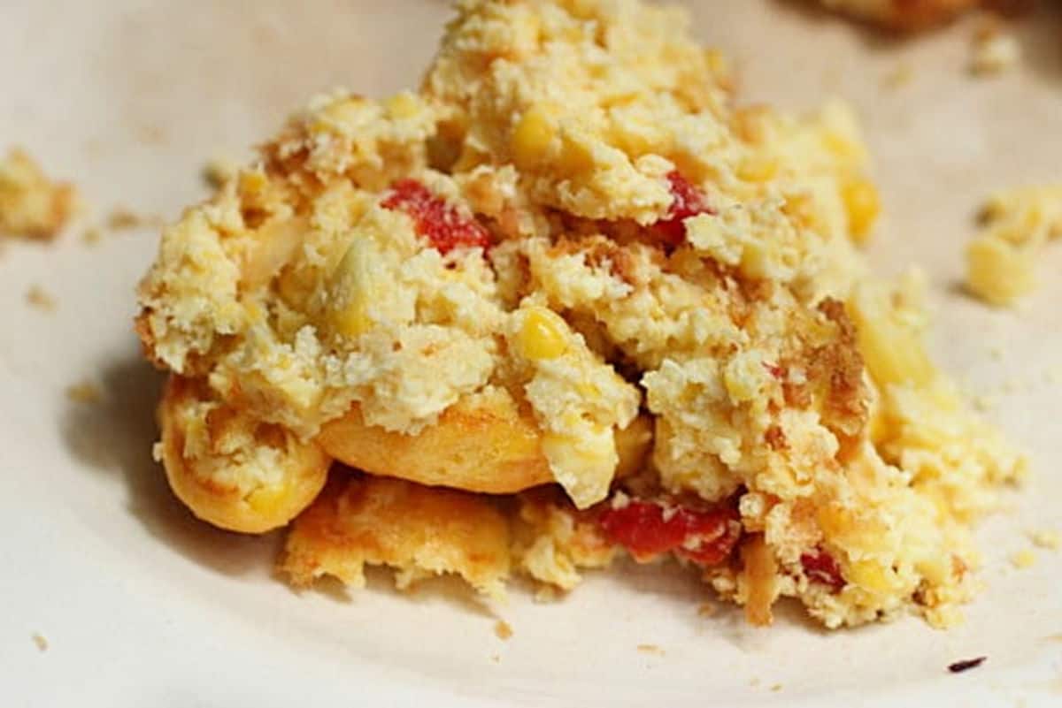 Serving of corn pudding with red peppers on a beige plate.