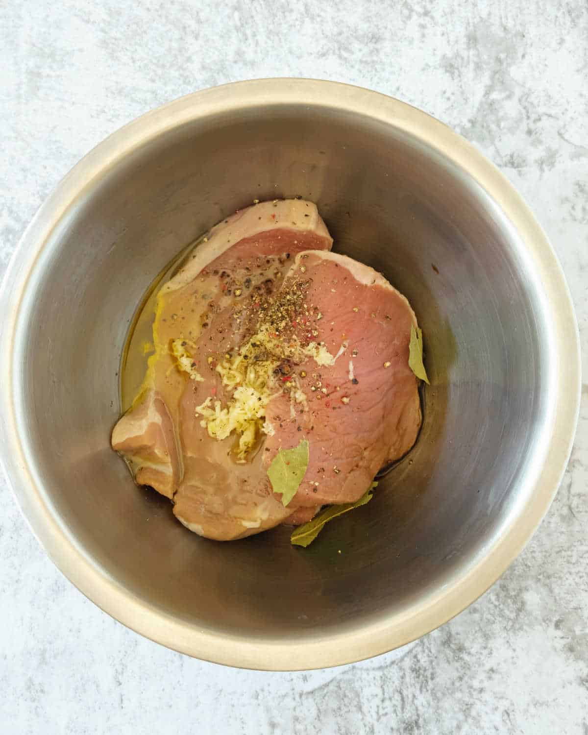 Metal bowl with meat marinating in olive oil and spices. Textured grey surface.