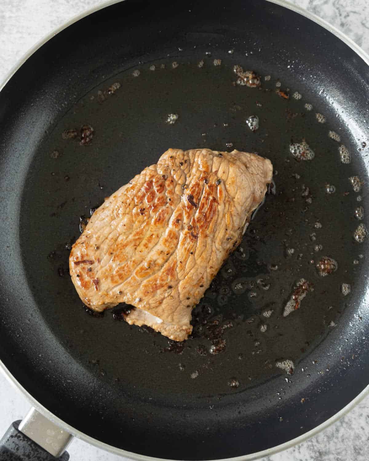Cooking a piece of meat in a black skillet.