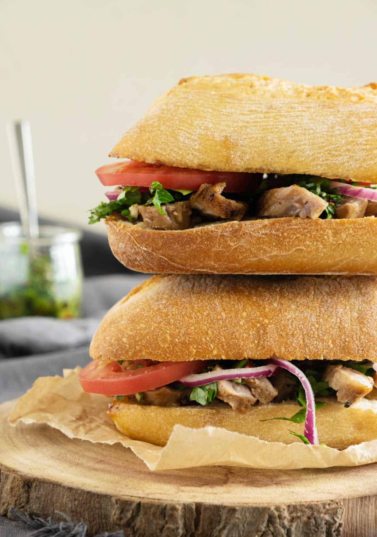 Stack of two steak, tomato and chimichurri sandwiches on a wood board. 