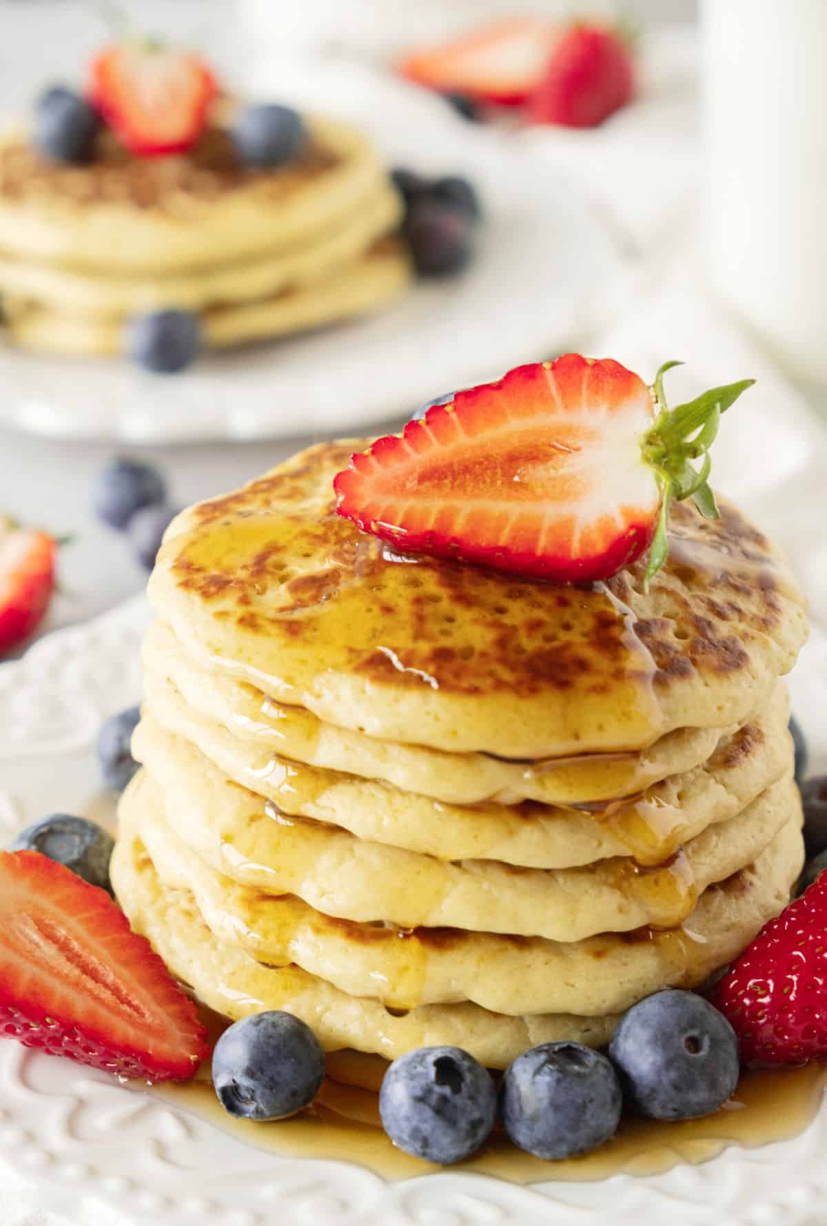 Pancakes in a stack with syrup and fresh berries on white plates.