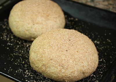 Black oven tray with two plump loaves of raw bread.