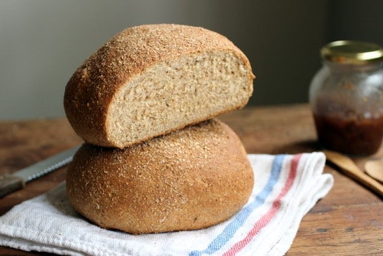 Two loaves of whole wheat bread on a kitchen towel on a wooden table.