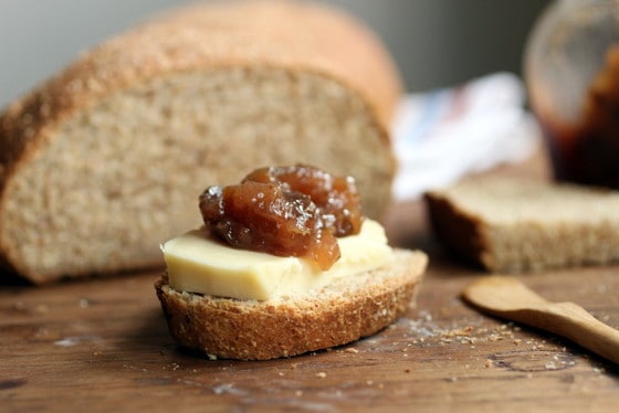 Close-up of slice of bread with hard cheese and jam on wooden table, cut bread on background