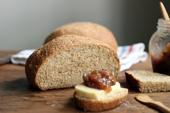 Cut round of whole wheat bread on wooden table, a slice with jam and cheese.