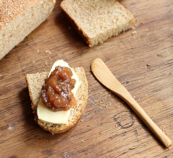 Slice of whole wheat bread with cheese and jam on wooden table, wooden spread knife