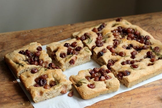 Slab of Focaccia with Roasted Grapes on parchment paper, wooden table