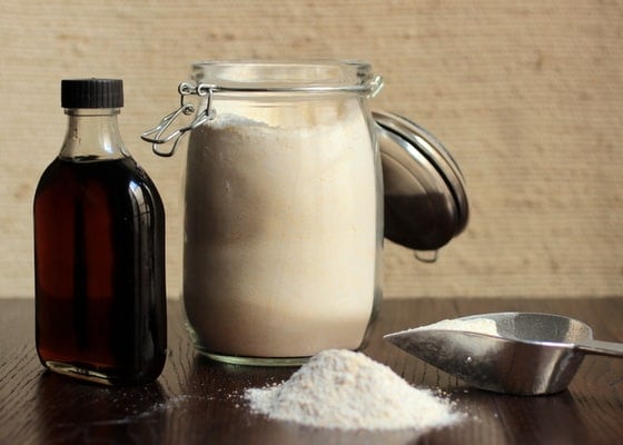 Cornmeal pancake mix in large jar and Maple Syrup bottle. Wooden tables and beige background. 