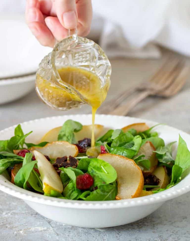 Pouring vinaigrette over pear arugula salad on white bowl plate