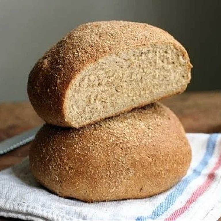Close up image of stacked whole wheat bread round loaves on a kitchen towel, top one is cut.