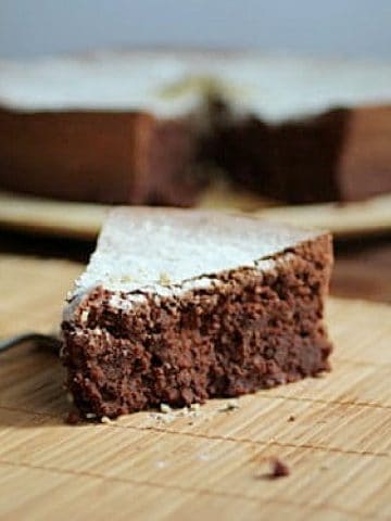 Single slice of chocolate cake on bamboo placemat with rest of cake in the background.
