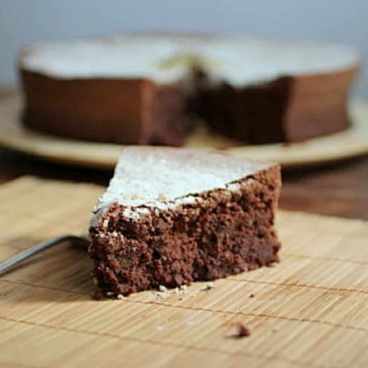 Single slice of chocolate cake on bamboo placemat with rest of cake in the background.