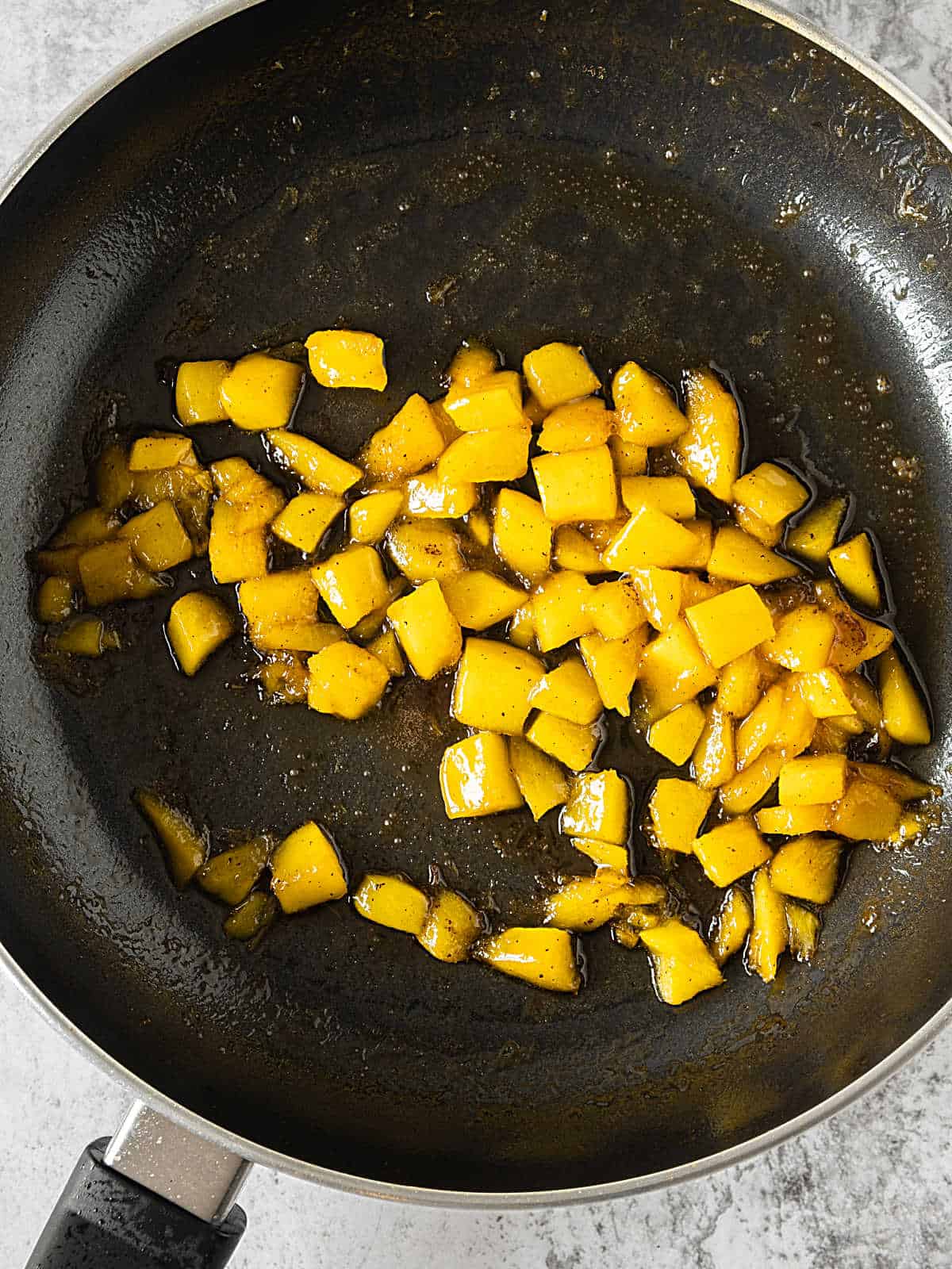 Diced mango cooked in a black skillet. 
