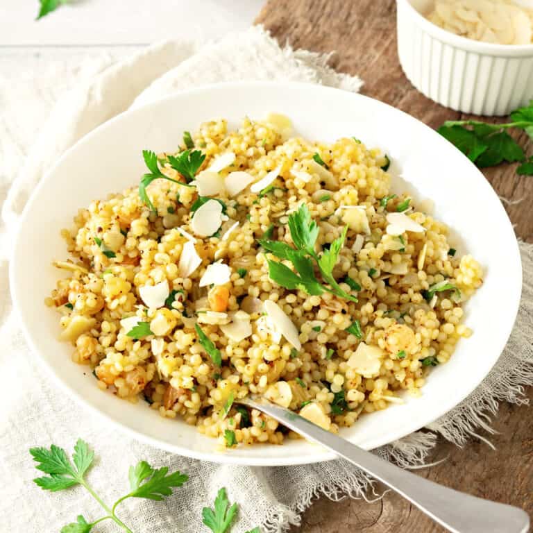 White plate with Moroccan-style couscous salad with parsley. White cloth, wooden board surface.