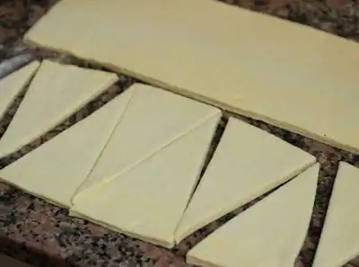 Triangles and rectangle of croissant dough on a brownish marble surface.