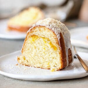 Close up slice of glazed mango coconut bundt cake on a white plate. Grey surface.