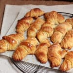 Batch of golden French croissants on white piece of paper over a wire rack.