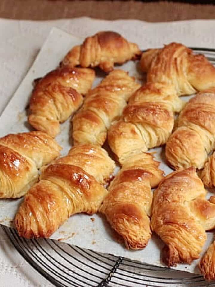 Batch of golden French croissants on white piece of paper over a wire rack.