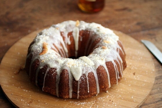Whole glazed bundt cake with coconut on a bamboo board on a wooden table. 