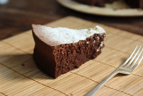 Slice of chocolate cake on a bamboo placemat with a silver fork. 