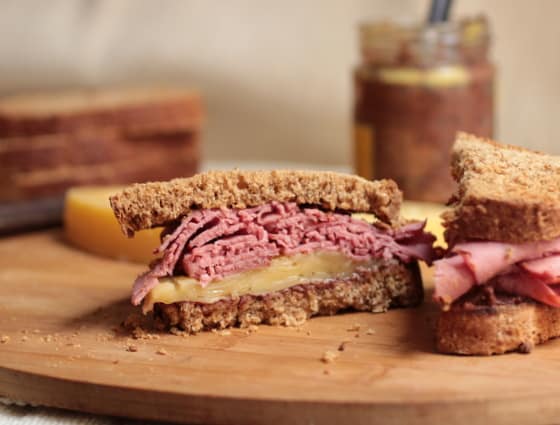 Half a pastrami and cheese sandwich on rye on a wooden board.