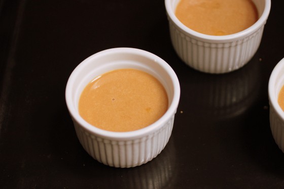 Black baking pan with white ramekins containing white chocolate custards before baking. 