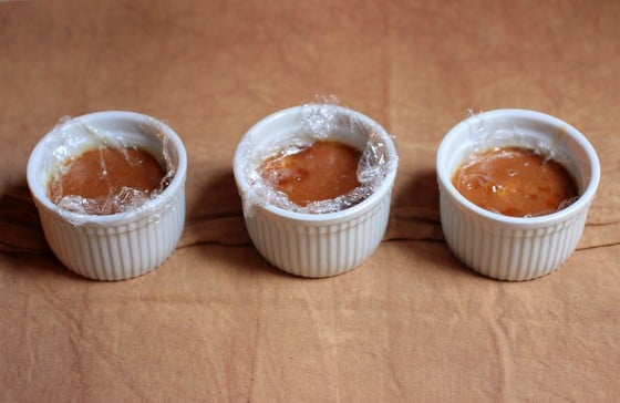 Beige cloth with three white ramekins on top containing white chocolate custard with plastic wrap on top. 