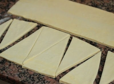 French croissants dough being cut into triangles. 