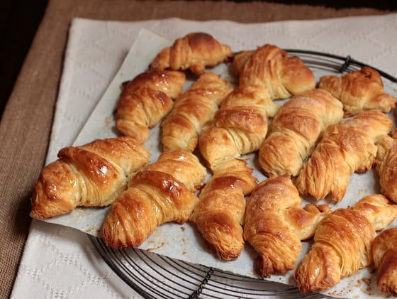  Several baked croissants on parchment paper on a wire rack. 