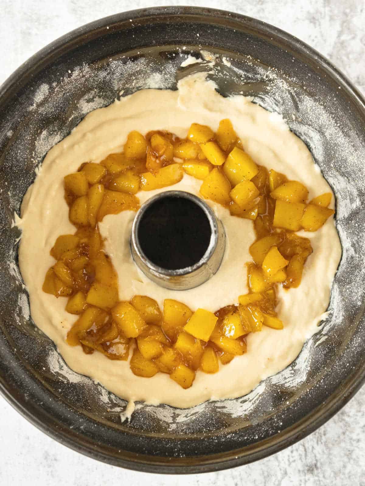 Assembling a coconut bundt cake with mango in the middle. Black cake pan. Grey surface.